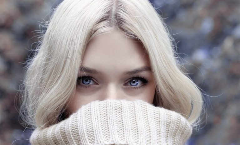 a woman with blue eyes and blonde hair covering her face with a sweater