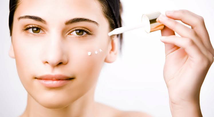 a woman applying a drop of cream on her face