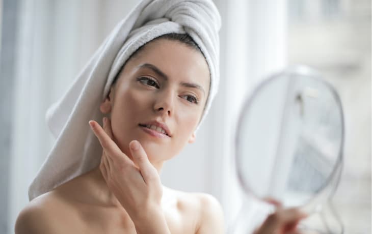 a woman with a towel on her head looking at her face