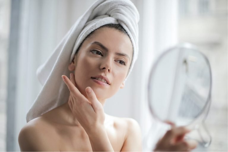 a woman with a towel on her head looking at her face